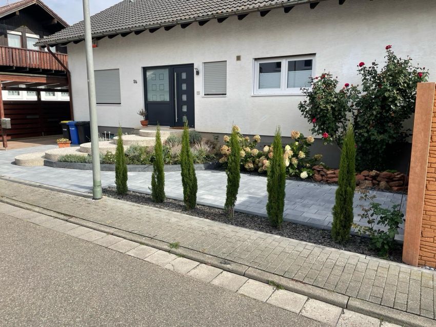 Am Hauseingang mit runder Treppe, Pflastersteinen und Lebensbäumen